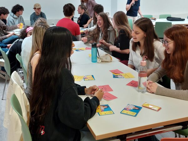 Auf dem Bild sitzen Schüler*innen am Tisch und besprechen Themen in Gruppen
